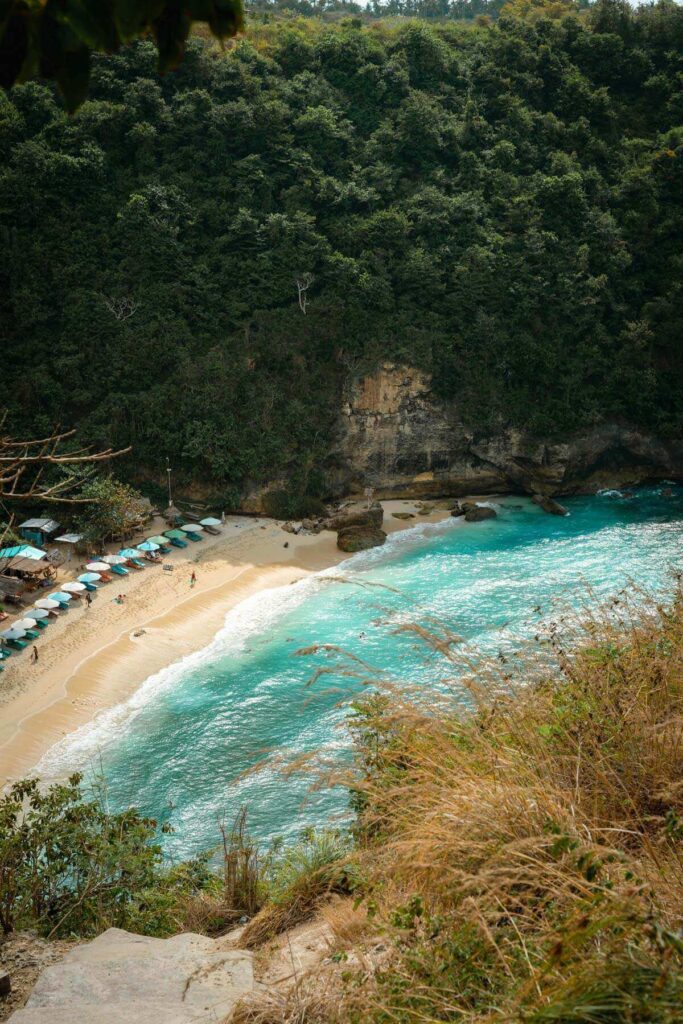 Atuh Beach and its colourful day beds and turquoise water visible from a viewpoint on top of a cliff.